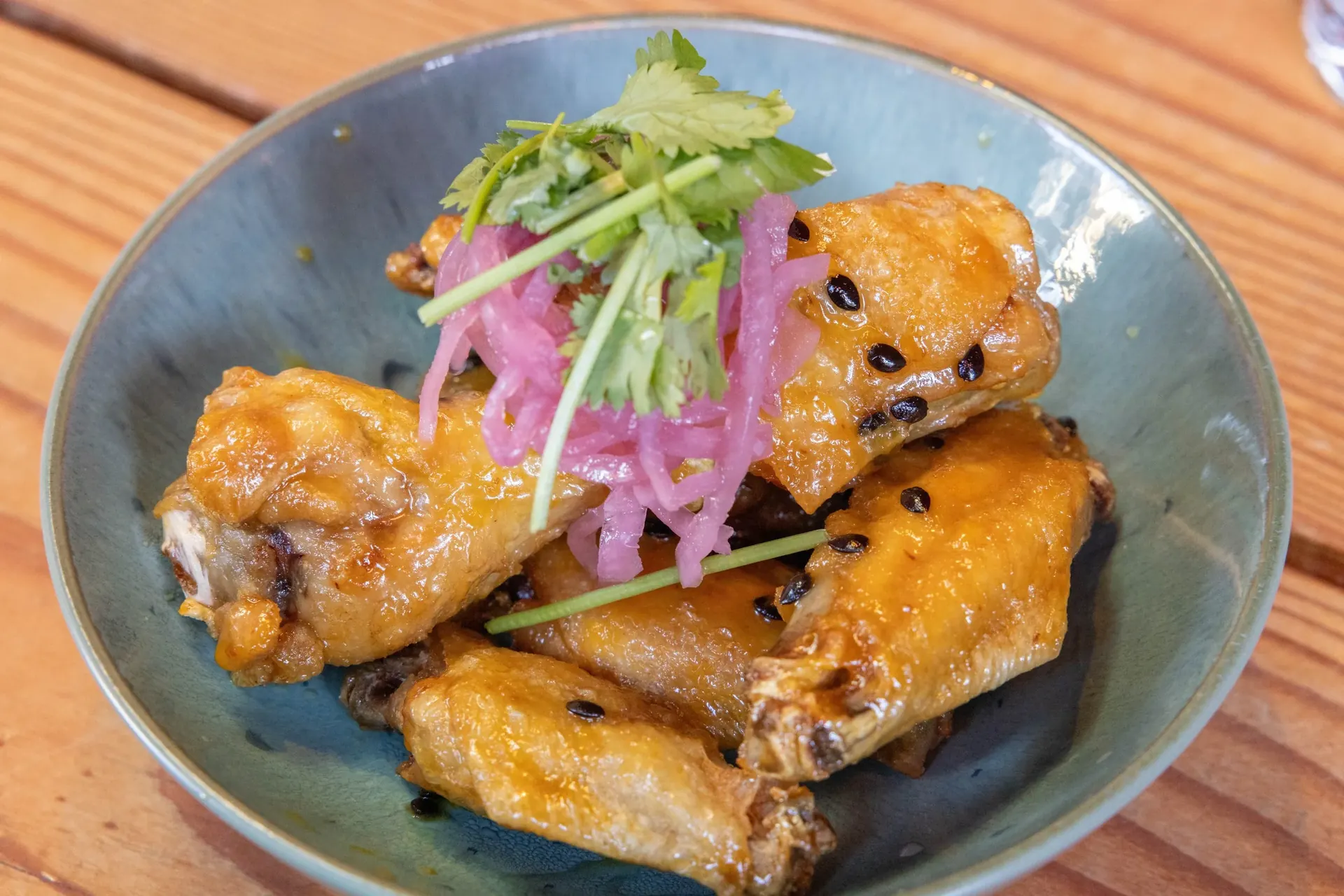 Xóm Wings — crispy whole chicken wings with pickled onions and cilantro in a ceramic bowl